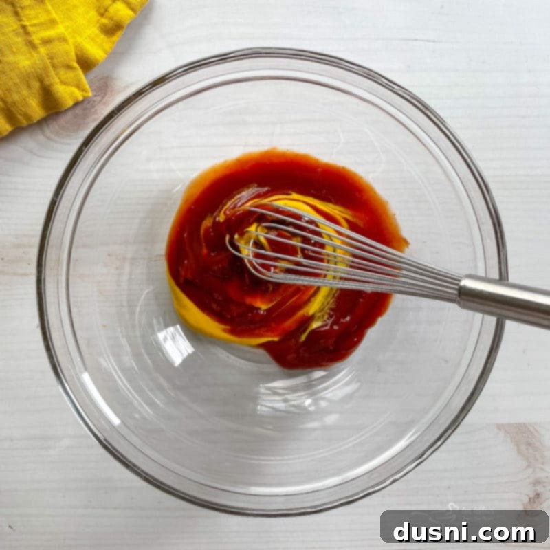 whisking ketchup and mustard in a small white bowl with a whisk, preparing the meatloaf glaze