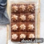 Mexican chocolate frosted brownies sliced and topped with cinnamon whipped cream, on a wood board.