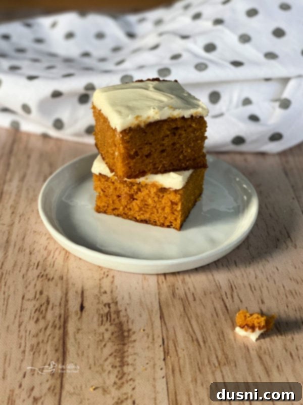 Moist Carrot Cake Bars Recipe Two soft carrot cake bars with thick, creamy vanilla cream cheese frosting on a white plate, ready to be served.