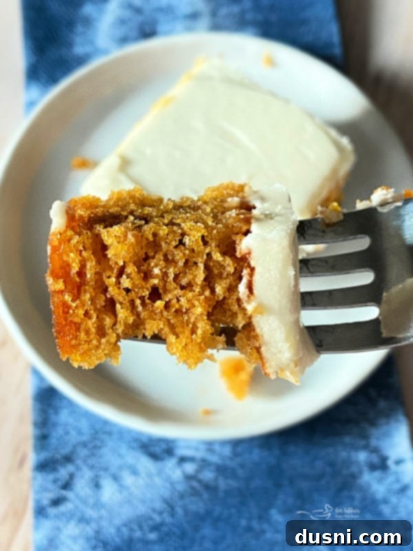 Carrot Cake Bars Recipe with Cream Cheese Frosting A fork holding a perfect bite of carrot cake bar, showcasing the moist cake and fluffy cream cheese frosting.