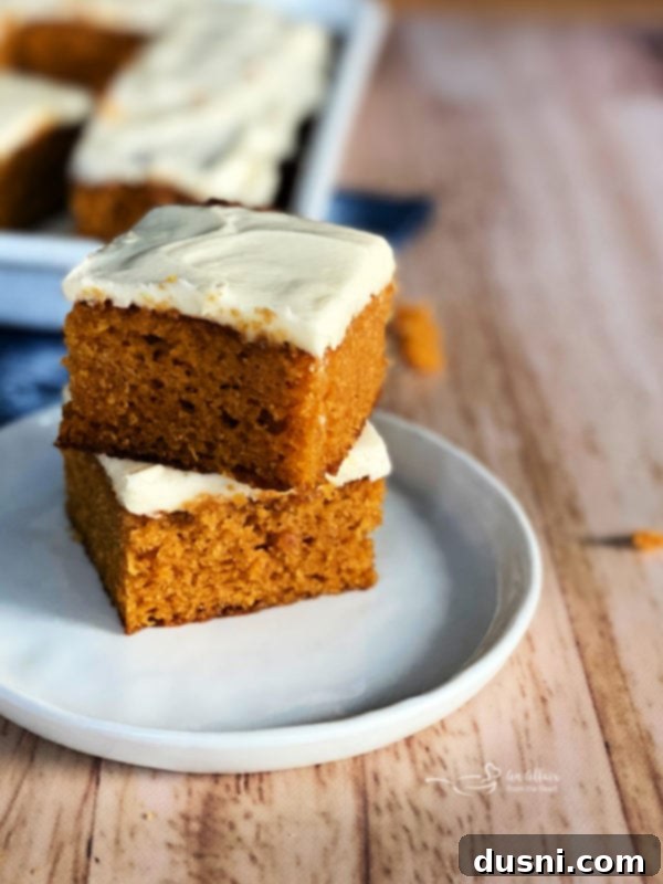 Carrot Cake Bars with Cream Cheese Frosting Two perfectly frosted carrot cake bars arranged on a pristine white plate, showcasing their inviting texture and generous cream cheese topping.