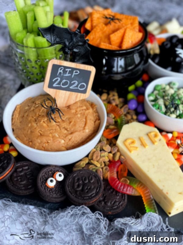 A Halloween snack board piled with spooky and sweet treats, perfect for a party, featuring themed cookies, dips, and candies.