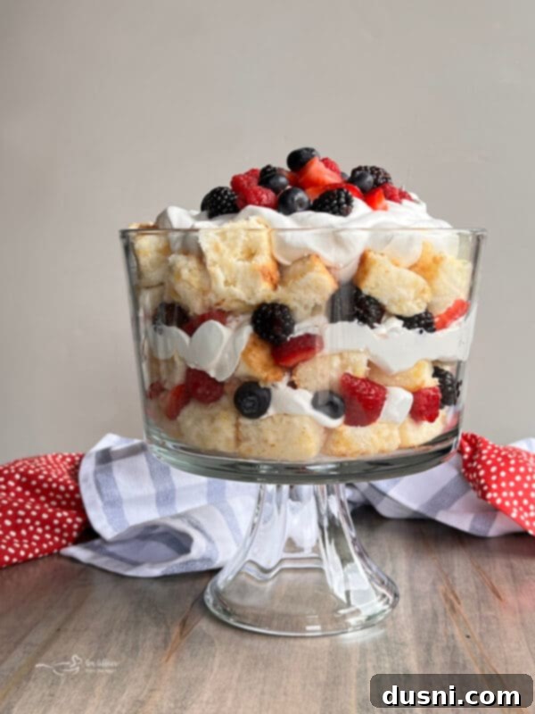 A vibrant Berry Trifle in a clear glass bowl, showcasing layers of angel food cake, fresh mixed berries, and whipped cream, garnished with mint.