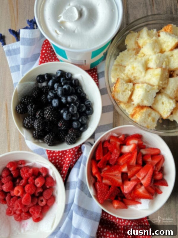 A top-down view of a Berry Trifle showing colorful layers of red strawberries, purple blackberries, and blue blueberries on top.