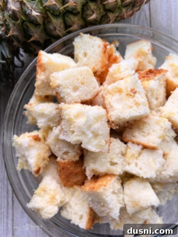 A serrated knife cutting angel food cake into cubes on a cutting board.