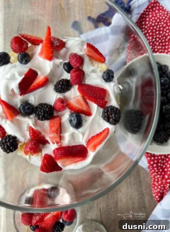 Whipped cream being spread evenly over the first layer of angel food cake in a trifle dish.