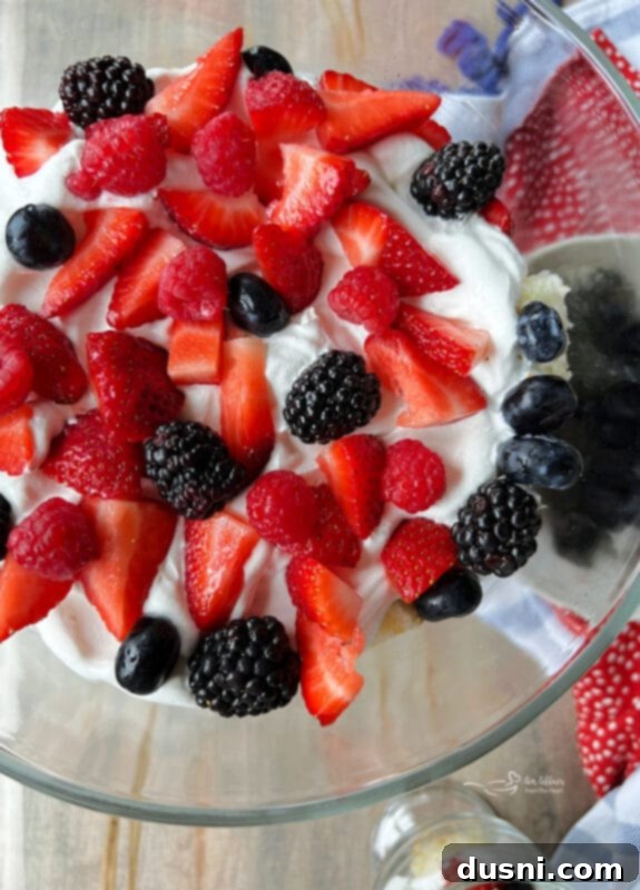 A layer of mixed berries over whipped cream and cake in a trifle dish, with the next layer being added.