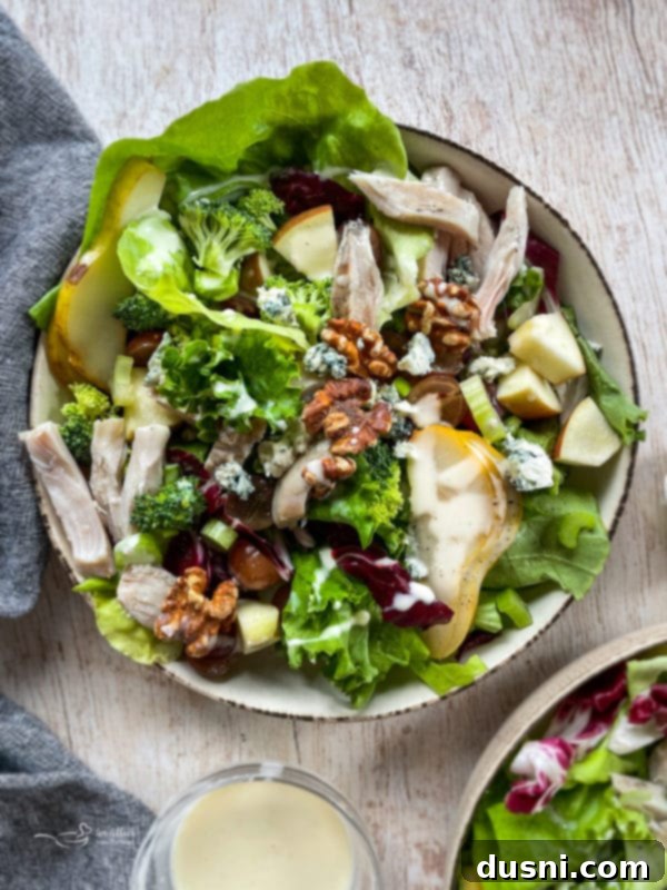 Waldorf Salad A vibrant Waldorf salad featuring tender grilled chicken, crunchy walnuts, juicy grapes, crisp apples, and fresh pears, all drizzled with a homemade vinaigrette dressing in a beautiful bowl.