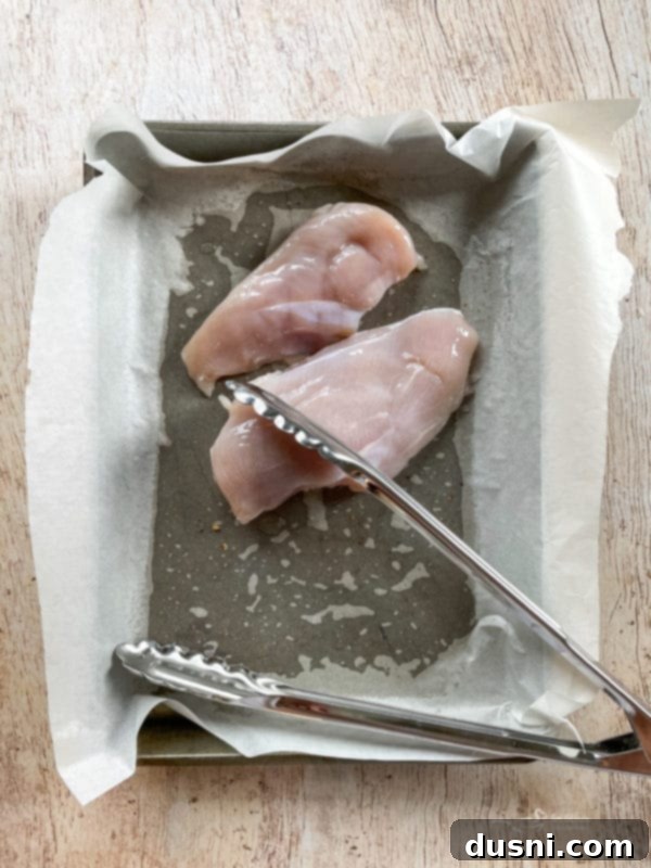 Chicken Waldorf Salad Raw chicken breasts, brined and ready for grilling, placed on a pan with tongs, highlighting the preparation stage for juicy, flavorful chicken.