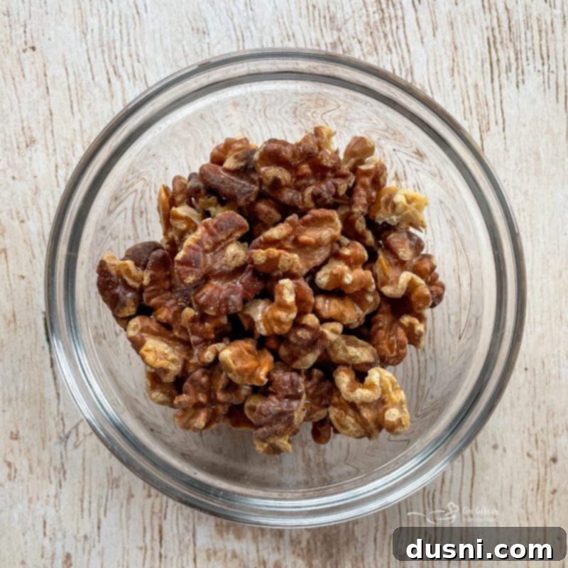 Chicken Waldorf Salad A bowl of freshly toasted walnuts, golden brown and fragrant, ready to be added as a crunchy topping to the Waldorf salad.
