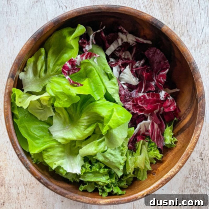 Waldorf Salad A large brown bowl filled with a fresh blend of green bib lettuce and red radicchio, forming the vibrant base of the salad.