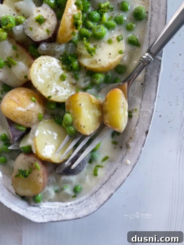 A dish of creamed new potatoes and peas with a fork, ready to be served as a comforting side.