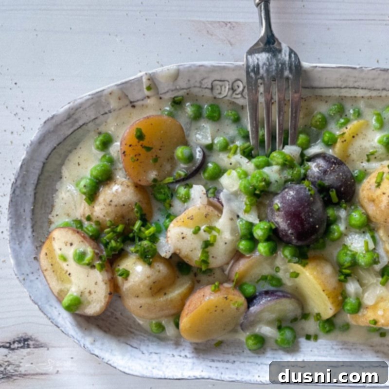 Close-up of a fork in a dish, showing creamy new potatoes and peas.