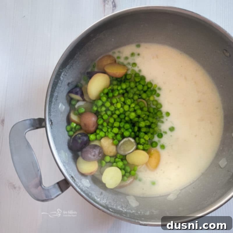 A pot filled with rich white sauce, tender peas, and new potatoes, ready to be combined.