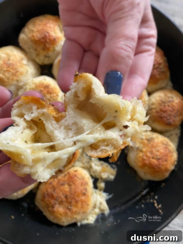 Hands pulling apart an Italian Cheese Bomb, revealing melted cheese inside
