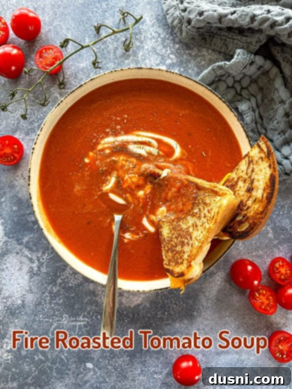 A beautifully presented bowl of creamy fire-roasted tomato soup, garnished with fresh herbs and a swirl of cream.