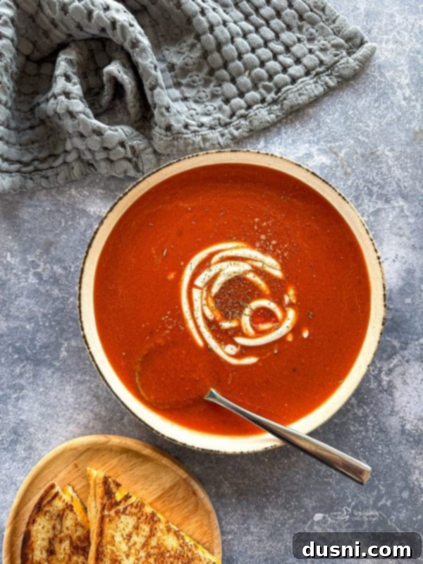 Close-up of creamy fire-roasted tomato soup in a white bowl with a spoon.