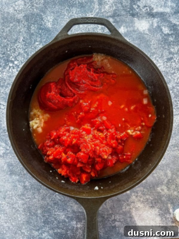 Canned tomatoes, tomato paste, tomato sauce, and chicken stock added to the Dutch oven with sautéed aromatics.