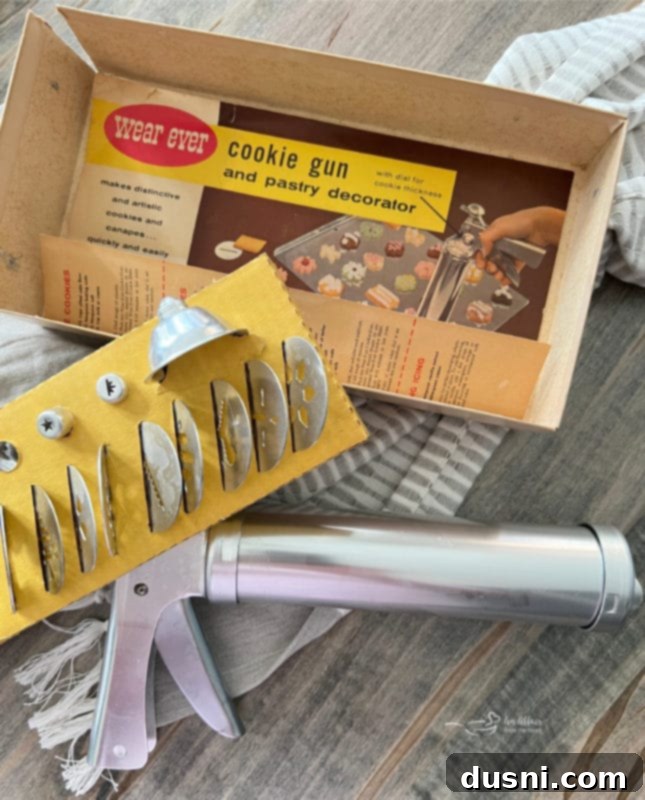 A classic metal cookie press, its box, and various disc designs