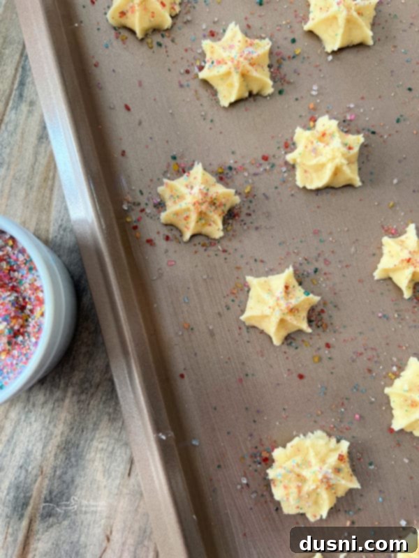 Freshly pressed spritz cookies on a baking sheet, ready for sprinkles