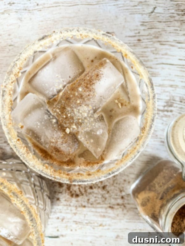 Velvet Pumpkin White Russian 2 Pumpkin White Russian Cocktail in a highball glass, garnished with a cinnamon stick and pumpkin pie spice on a wooden surface.