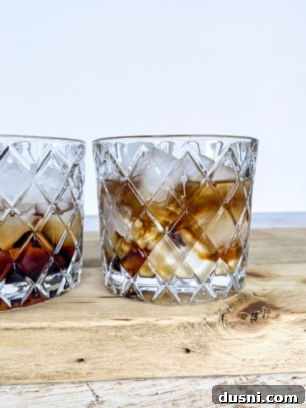 Velvet Pumpkin White Russian 7 A hand pouring pumpkin spice creamer into a glass containing Kahlua, vodka, and ice, creating a layered Pumpkin White Russian.