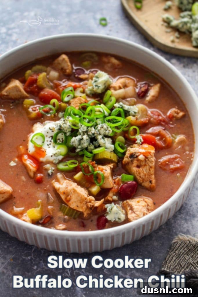 Hearty Slow Cooker Buffalo Chicken Chili 15 Hero shot of a richly garnished bowl of Slow Cooker Buffalo Chicken Chili, with a spoonful of chili being lifted.
