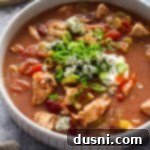 Hearty Slow Cooker Buffalo Chicken Chili 17 Close up of a bowl of Slow Cooker Buffalo Chicken chili topped with blue cheese, green onions, sour cream and hot sauce.