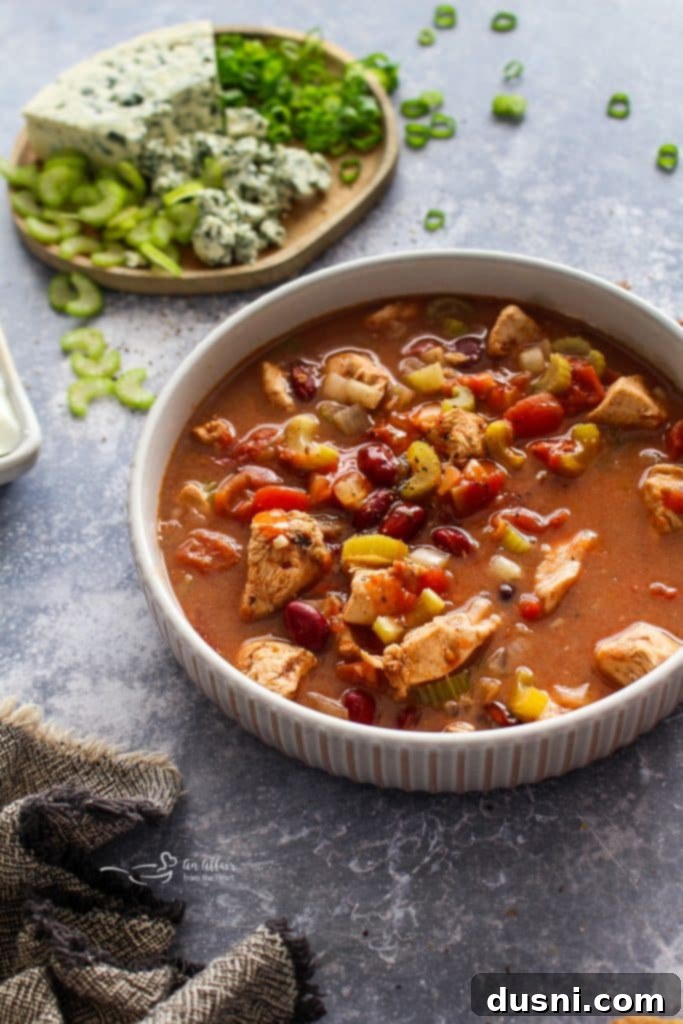 Hearty Slow Cooker Buffalo Chicken Chili 3 Close-up of a bowl of creamy Slow Cooker Buffalo Chicken Chili with visible chicken, beans, and celery, garnished with fresh herbs.