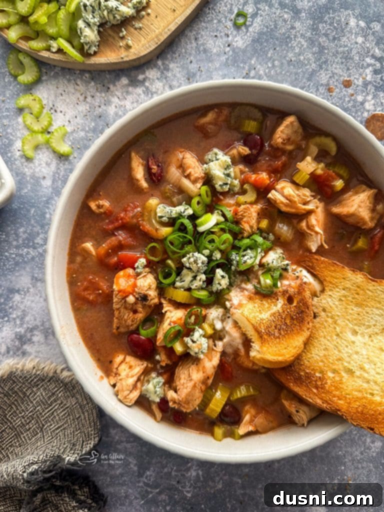 Hearty Slow Cooker Buffalo Chicken Chili 9 A beautifully presented bowl of Slow Cooker Buffalo Chicken Chili, topped with an array of fresh and creamy garnishes, ready to eat.