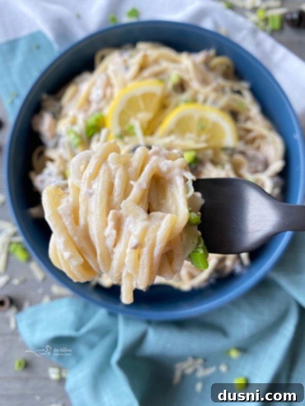 Close-up of tuna spaghetti wrapped around a fork over a bowl, showcasing the creamy sauce and ingredients