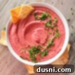 white bowl with pink hummus and parsley with chips