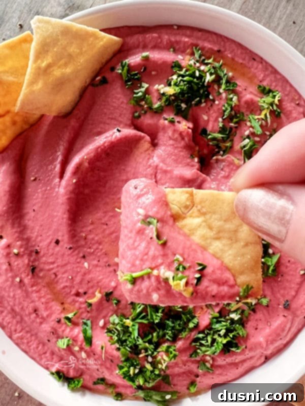 white bowl of pink hummus with crackers and parsley
