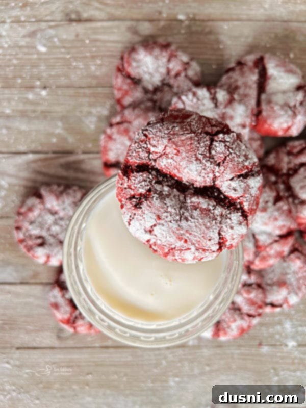 Red Velvet Crinkle Cookies A red velvet cookie being dipped into a glass of milk, highlighting its soft texture.
