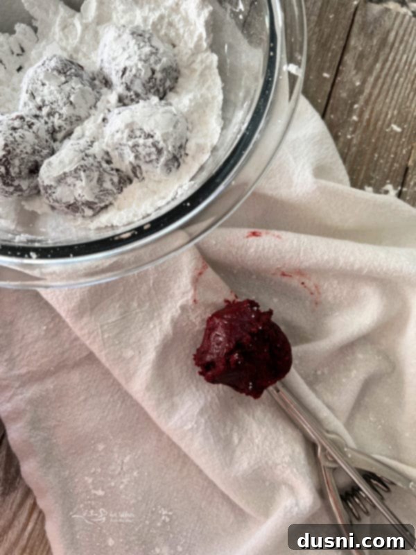 Red Velvet Cookies Rolling red velvet cookie dough in a bowl of powdered sugar to create the crinkle effect.