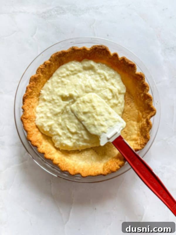 Step-by-step image: warm coconut custard filling being poured into a baked pie crust