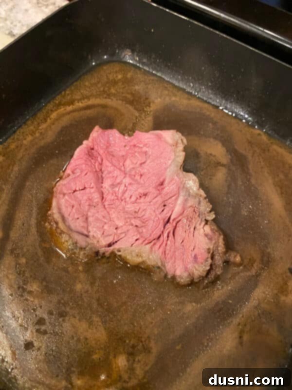 Sliced prime rib being warmed in an electric skillet with au jus