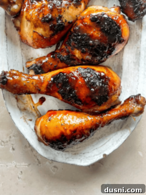 Sweet and sticky grilled chicken legs on a white plate with lemon slices