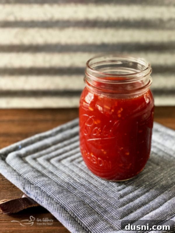 Jar of Homemade Barbecue Sauce on a grey potholder, with a spoon for tasting
