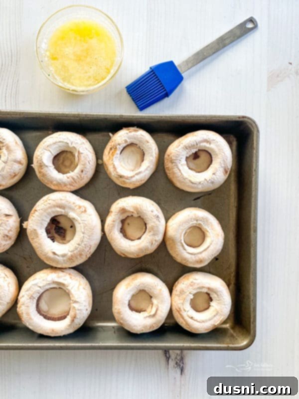 Stuffed Mushrooms Recipe Cleaned mushroom caps arranged on a baking sheet, brushed with butter and ready for stuffing.