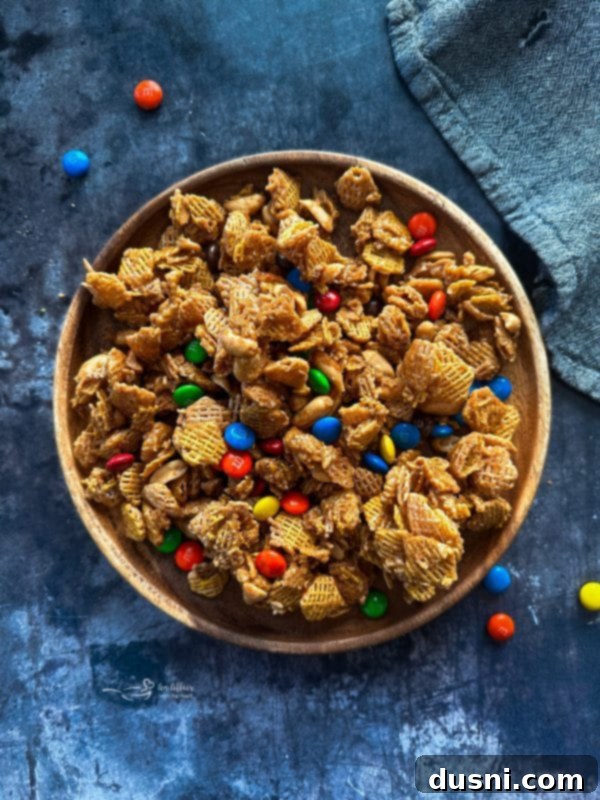 A large bowl of Candy Coated Crispix Mix, featuring caramel-coated Crispix cereal, peanuts, and red and green M&Ms, ready for holiday festivities.