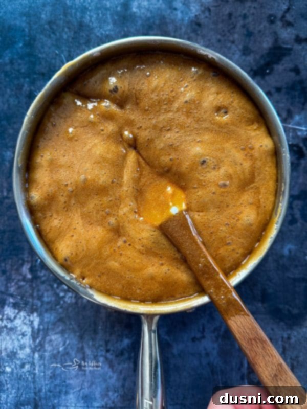 Caramel mixture boiling in a saucepan on the stovetop, achieving a deep golden color.