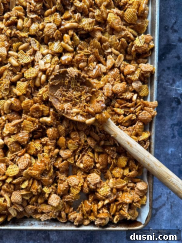 Crispix cereal and peanuts being tossed with the caramel coating in a large mixing bowl.