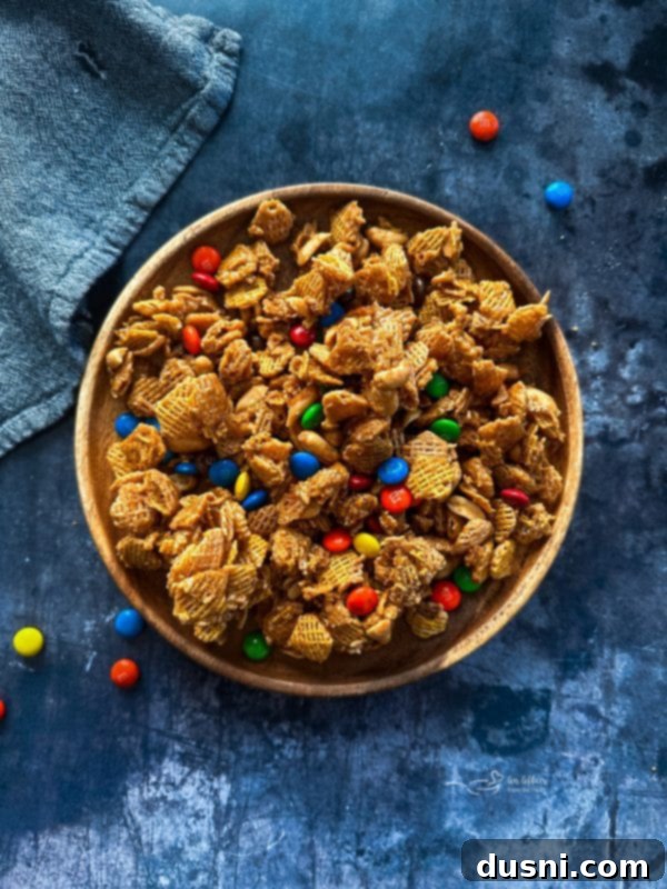 Close-up of Candy Coated Crispix Mix, highlighting the shiny caramel glaze on the cereal and the mix of colorful M&Ms and peanuts.