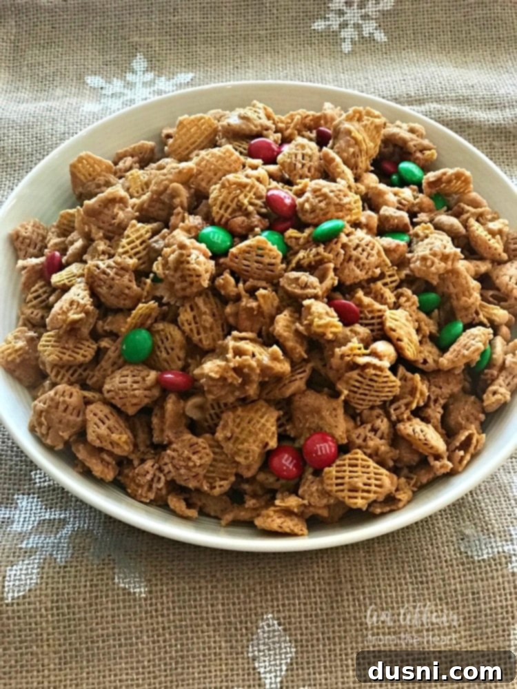 A white bowl filled with Candy Coated Crispix Snack Mix, showcasing the golden caramel, peanuts, and colorful M&Ms.