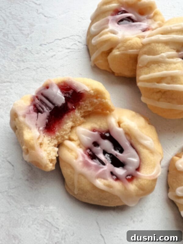 Raspberry Almond Shortbread Jewels 2 Freshly baked almond raspberry thumbprint cookies with glistening jam and glaze on a white plate