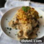 Comforting Stuffed Pork Chops 3 baked pork chop on plate with stuffing and herbs on top with mushroom gravy