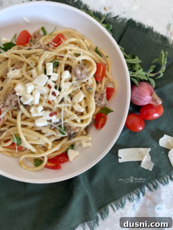Top-down view of a white plate holding pasta with Italian sausage and tomatoes, a hearty meal idea.