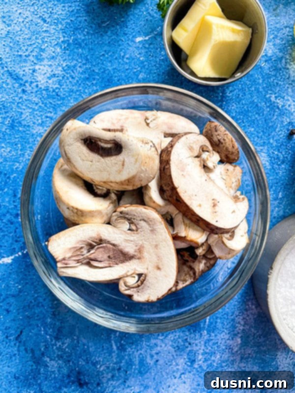 A bowl of fresh sliced mushrooms with a pat of butter, ready for sautéing.