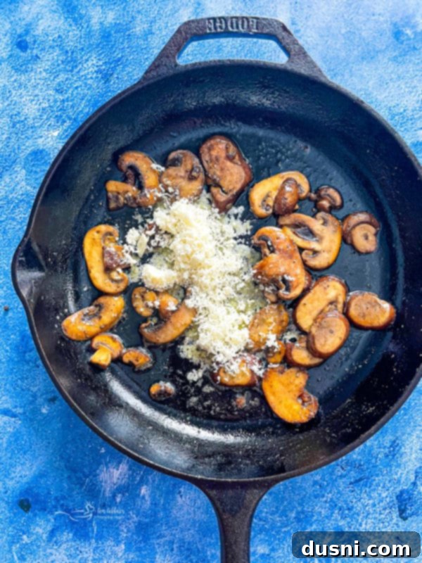 A skillet with sautéed mushrooms, joined by Parmesan cheese, butter, and olive oil, beginning to form the sauce.